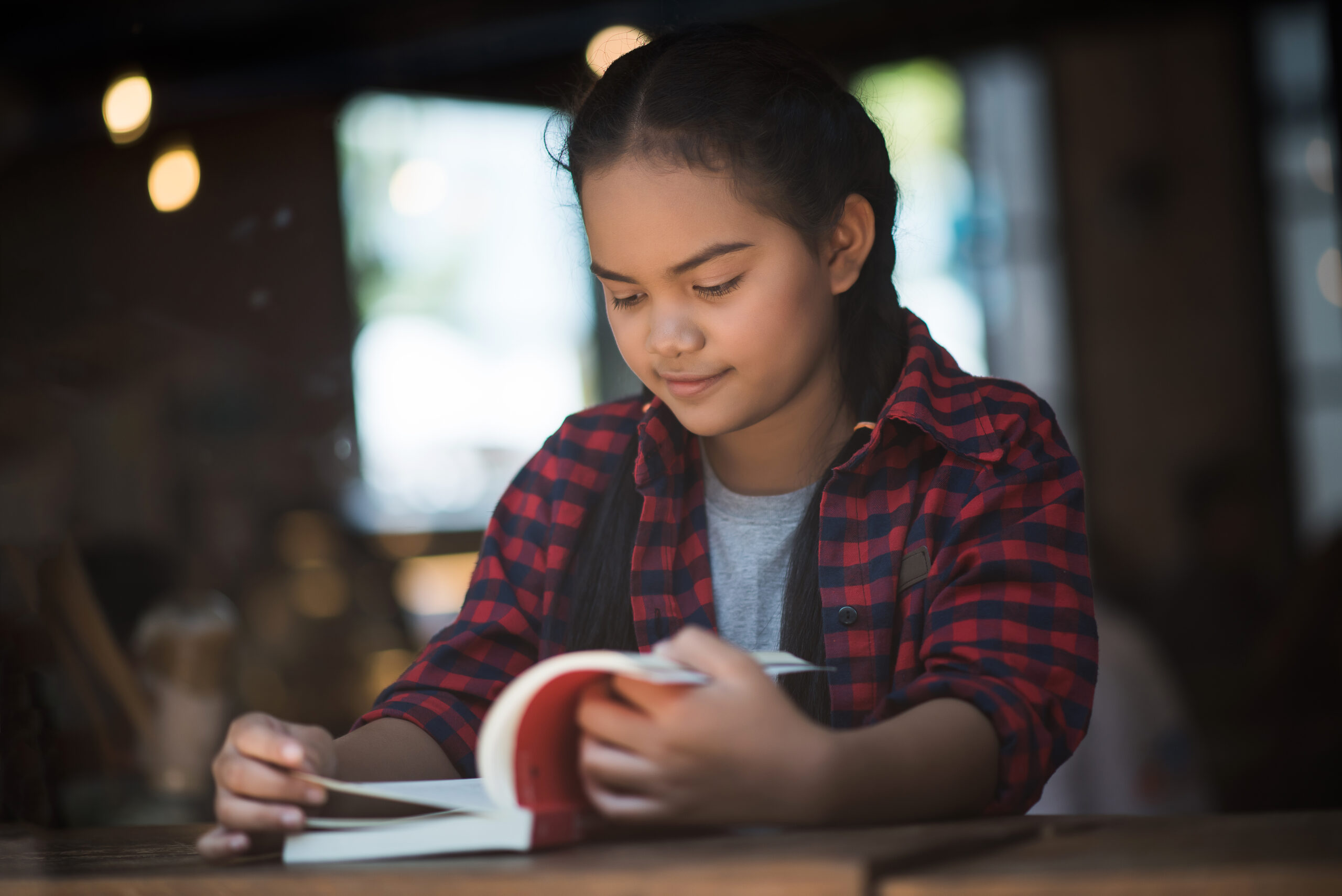 young woman reading book sitting indoor in urban cafe.